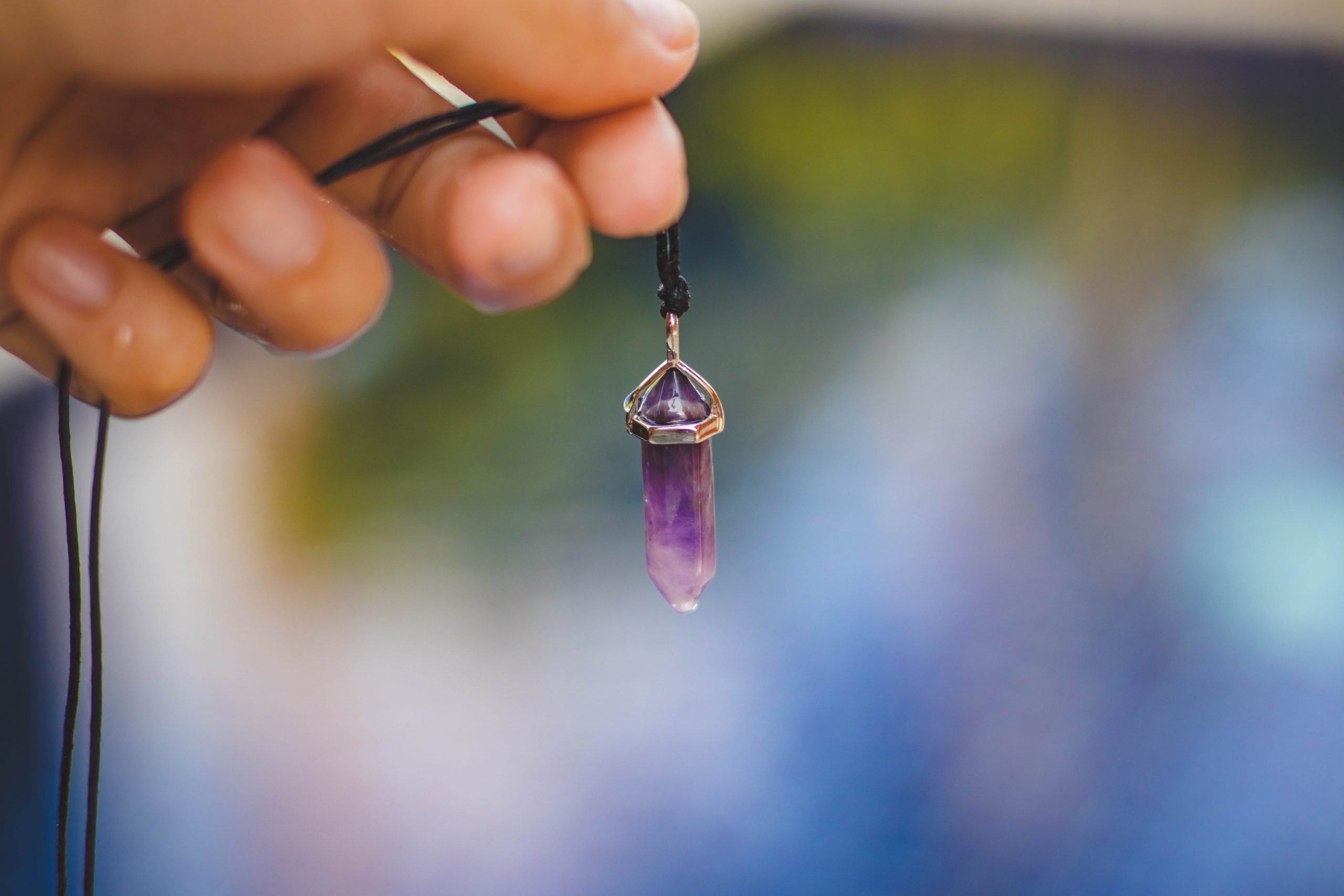 Canva - Person Holding Black Necklace With Purple Stone Pendant