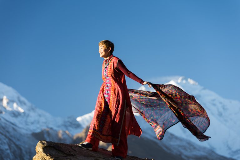 Canva - Woman in Orange Dress Standing on Top of Rock Cliff Holding Scarf Near Mountain Covered With Snow