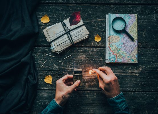 old letters with vintage map and burning match in hands on a wooden table.